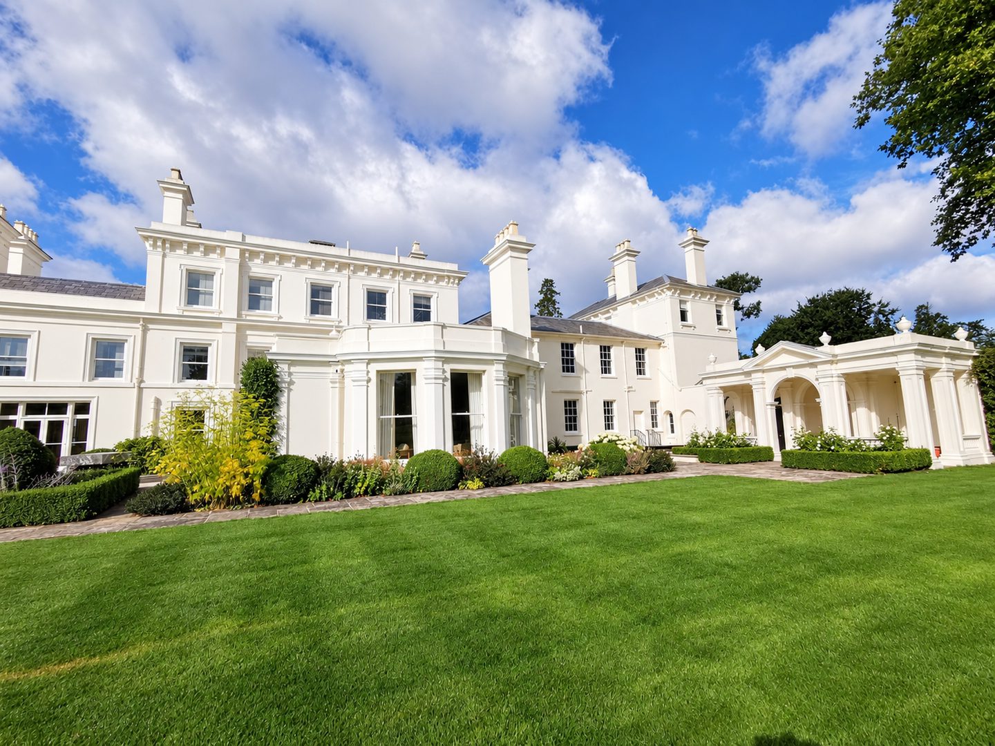 Ashurst, the restored white stucco façade and colonnaded wings seen across the front lawn