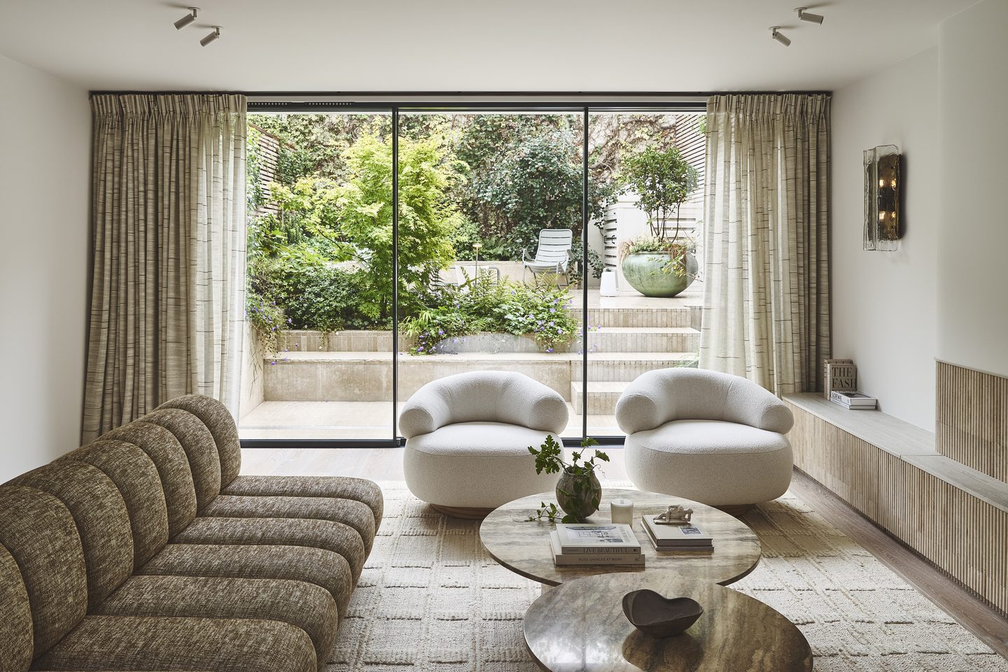 Reception room with curved bouclé seating and full-height doors opening to the garden