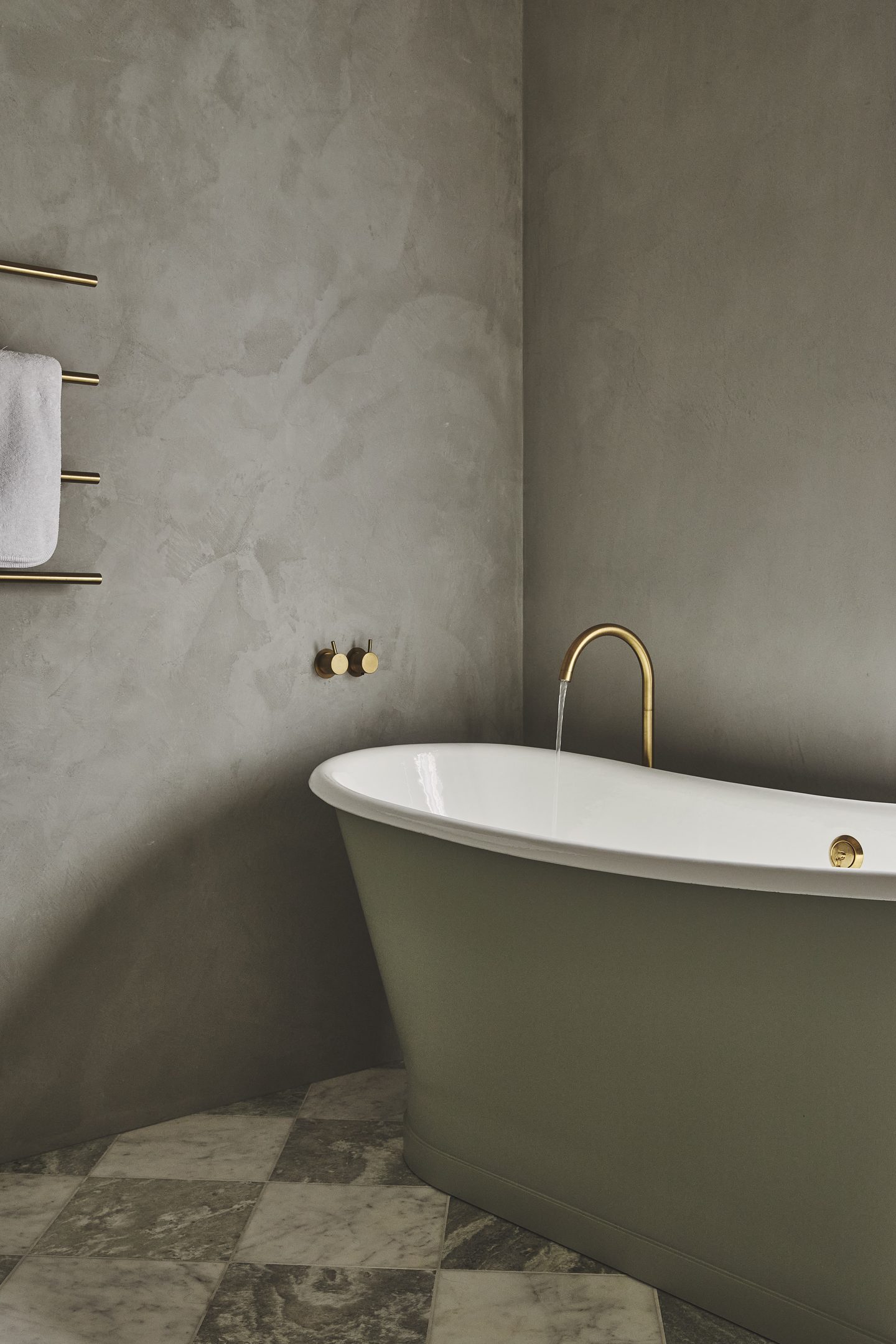 Freestanding green bath against microcement walls and chequerboard marble