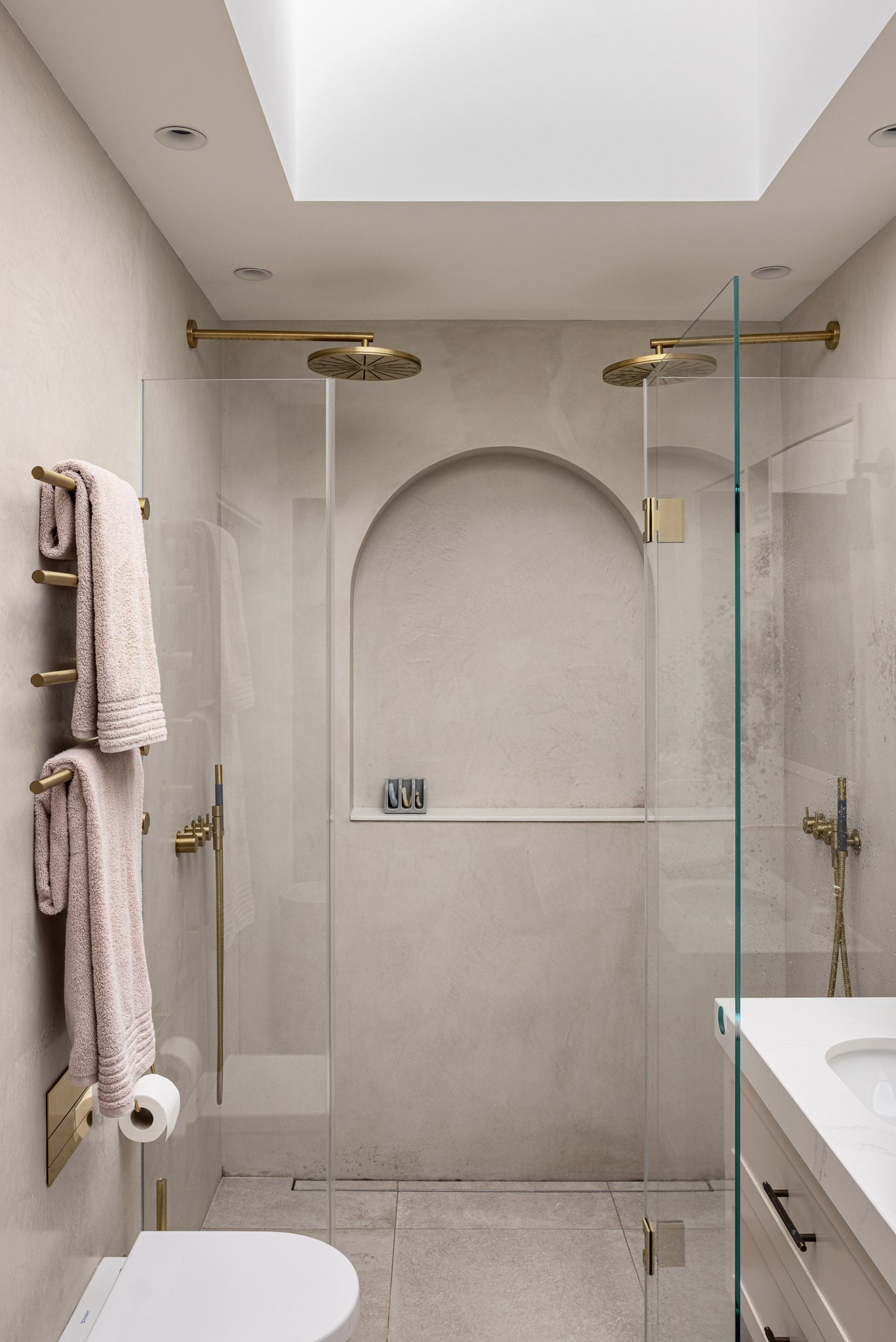 Shower room with arched niche and brass fittings beneath a skylight